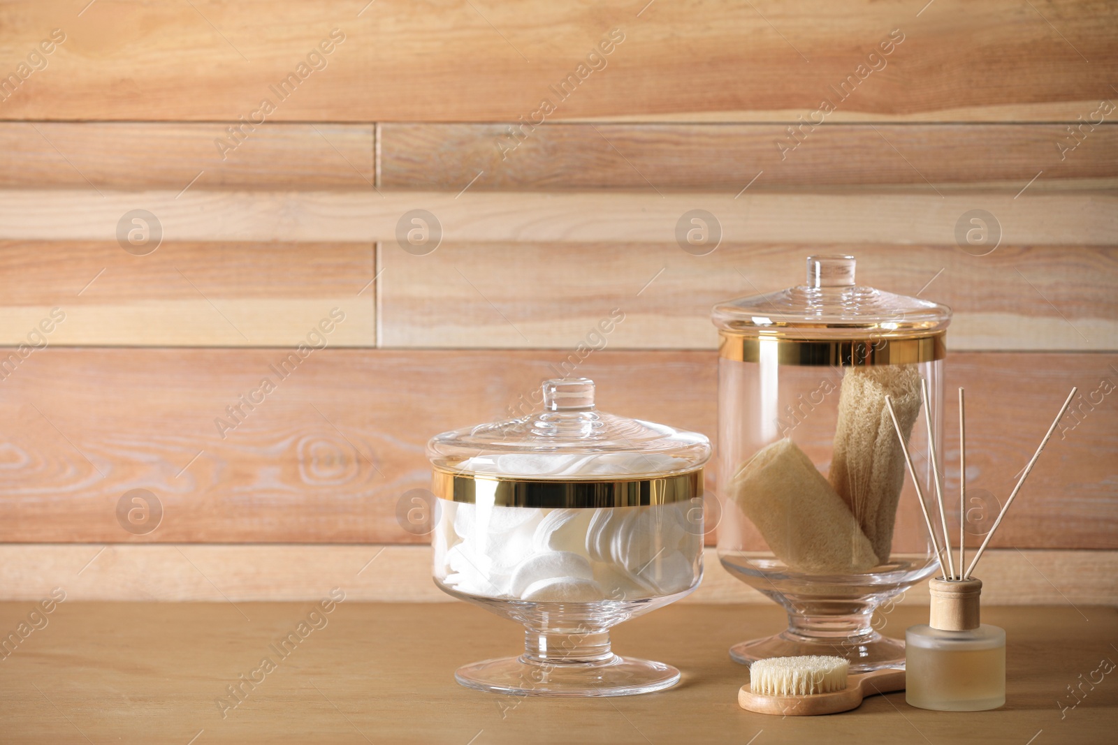 Photo of Reed air freshener, jars with cotton pads and loofah sponges on table against wooden background. Space for text