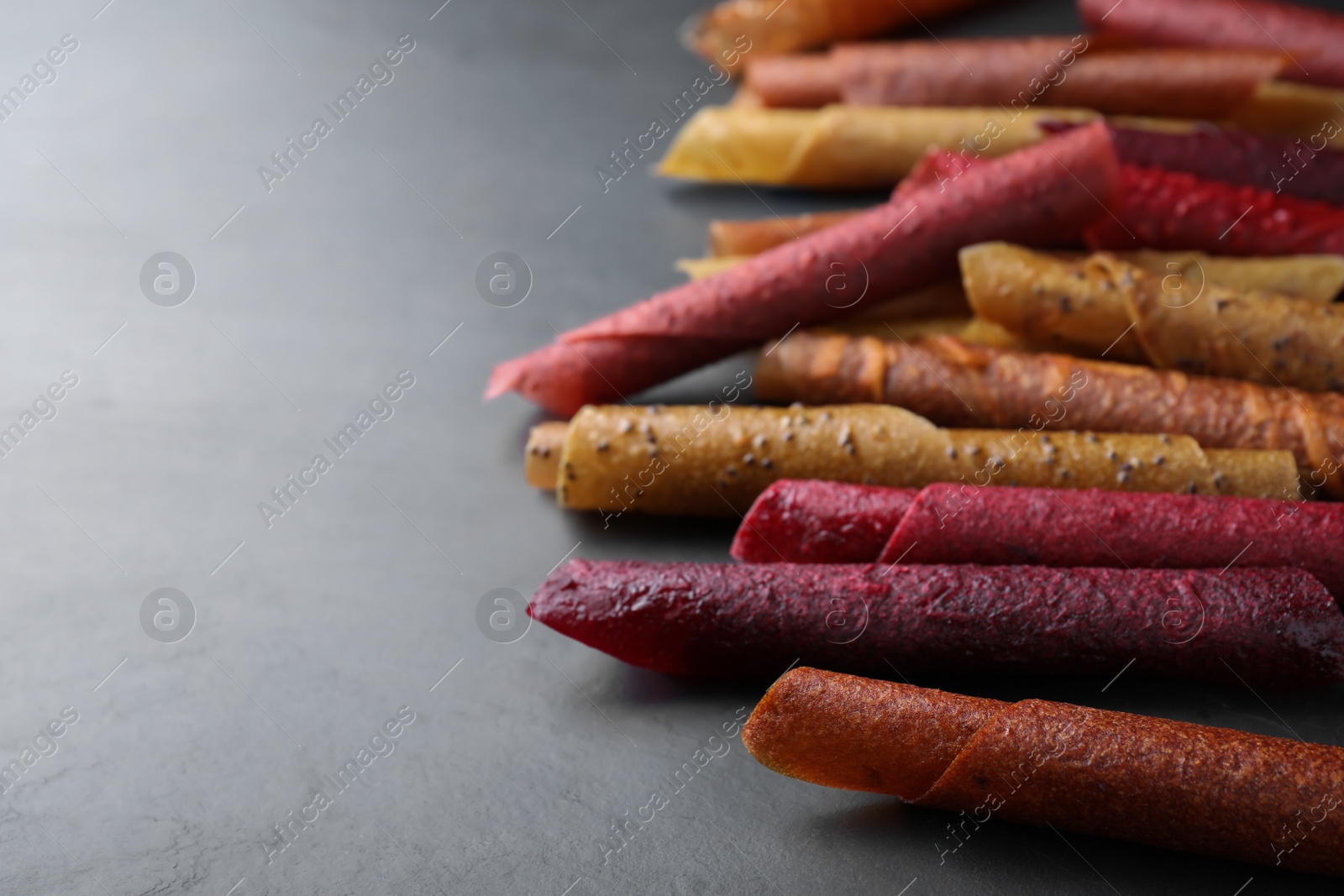 Photo of Delicious fruit leather rolls on black table, closeup