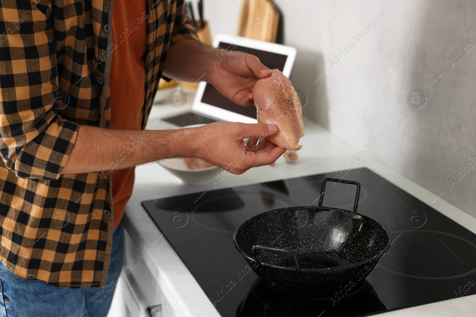 Photo of Man putting chicken fillet into frying pan while watching online cooking course via laptop in kitchen, closeup