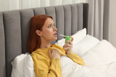 Photo of Young woman using throat spray in bedroom