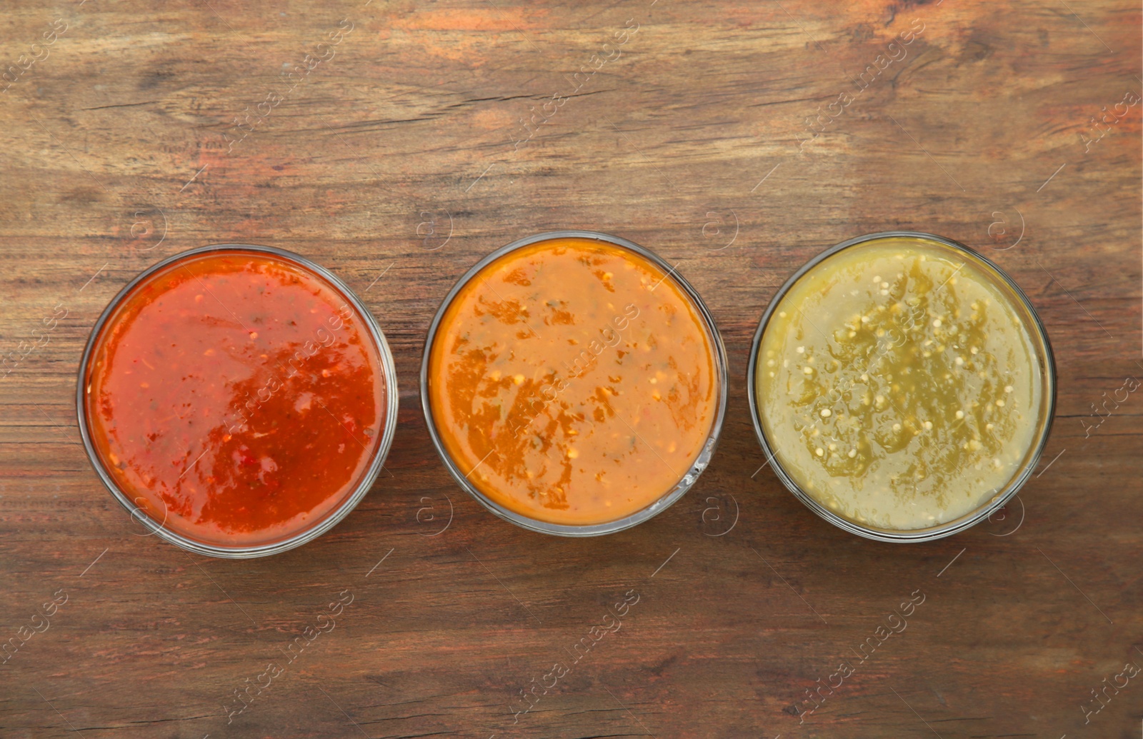 Photo of Different tasty salsa sauces on wooden table, flat lay