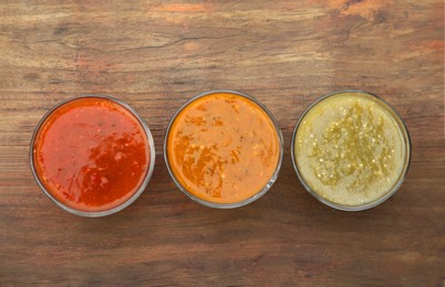 Different tasty salsa sauces on wooden table, flat lay