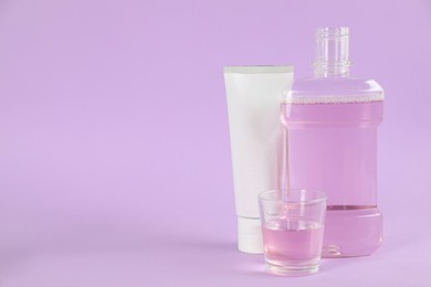 Photo of Mouthwash and toothpaste on violet background, space for text
