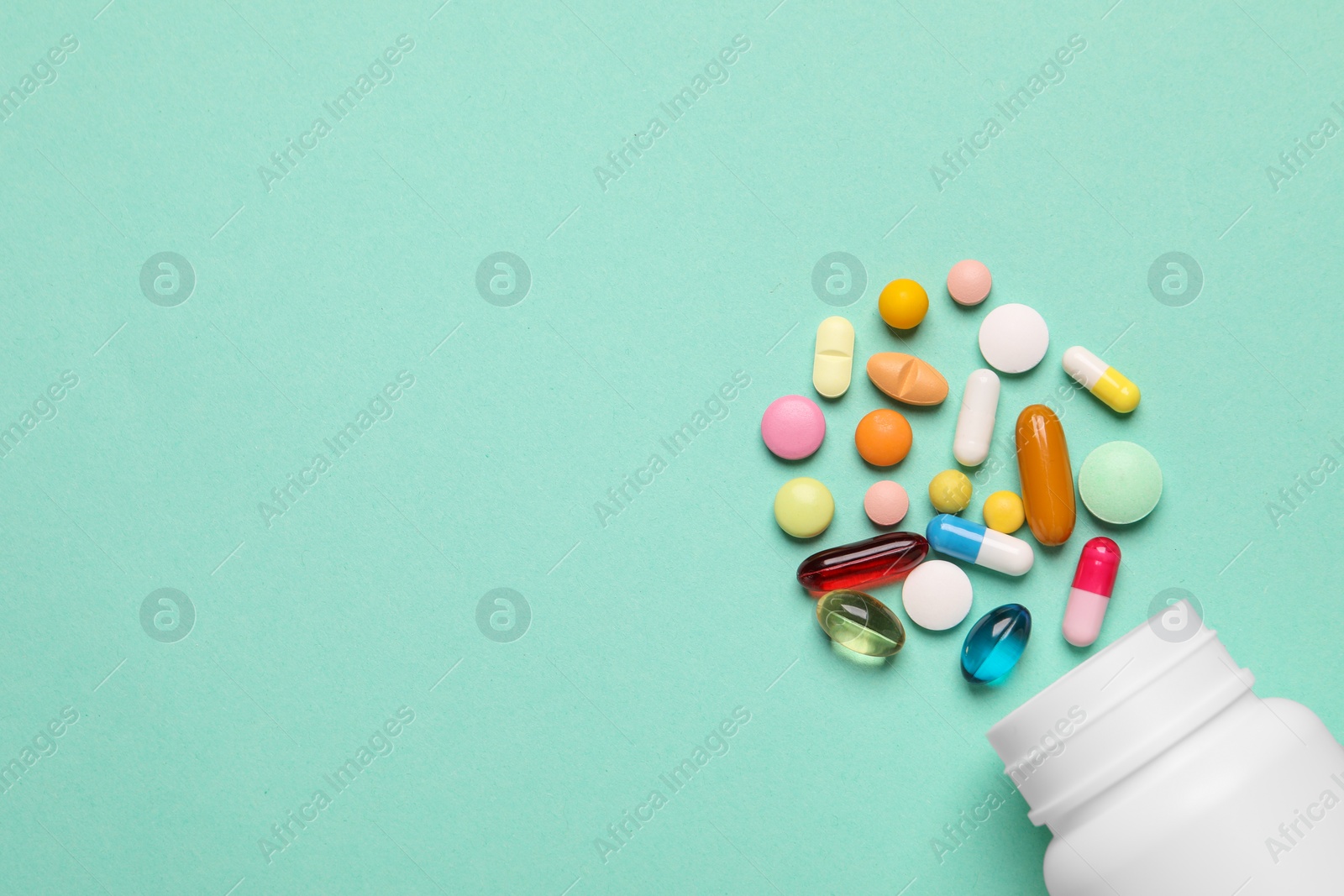 Photo of Plastic medical bottle with many different pills on turquoise background, flat lay. Space for text