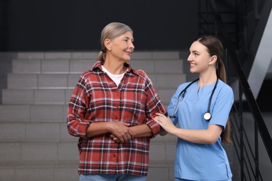 Photo of Young healthcare worker assisting senior woman on stairs indoors