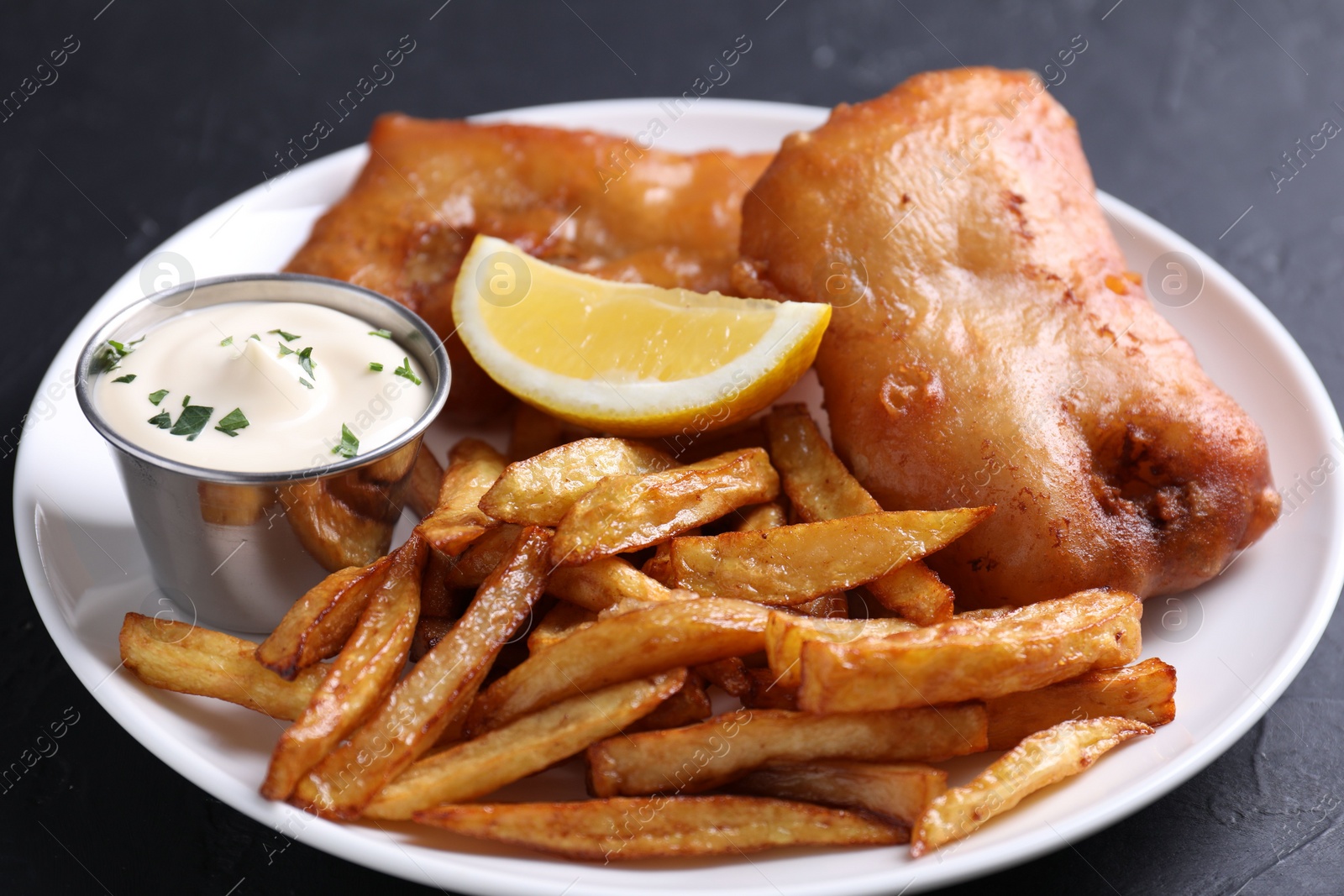 Photo of Tasty fish, chips, lemon and sauce on black table, closeup