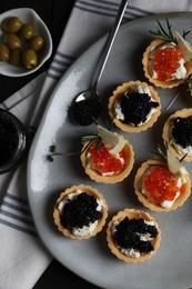 Delicious tartlets with red and black caviar served on dark table, flat lay