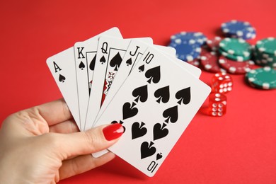 Photo of Woman holding playing cards with royal flush combination at red table, closeup