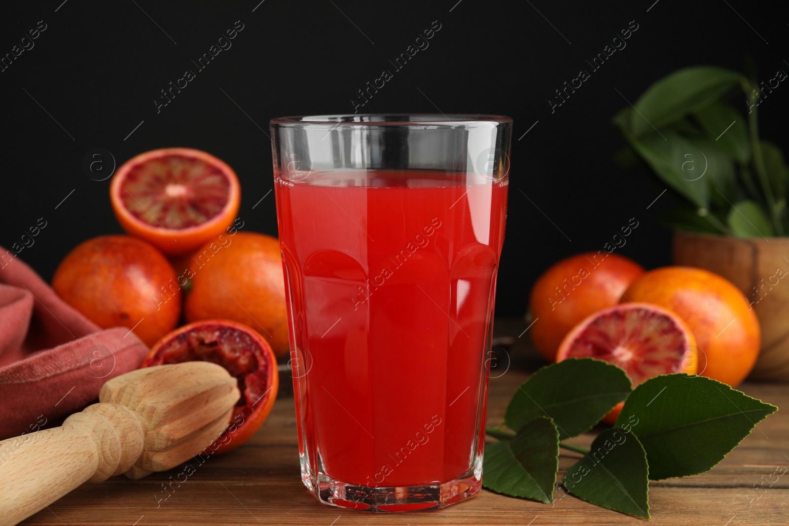 Photo of Tasty sicilian orange juice in glass, fruits and squeezer on wooden table