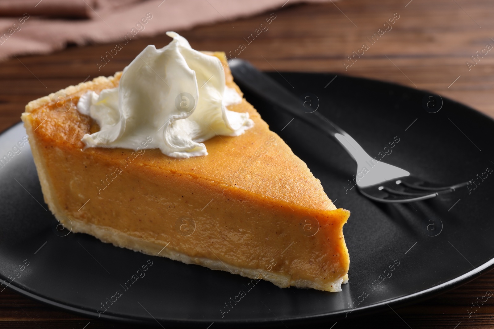 Photo of Piece of delicious pumpkin pie with whipped cream and fork on table, closeup