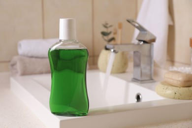 Photo of Fresh mouthwash in bottle on sink in bathroom, closeup. Space for text