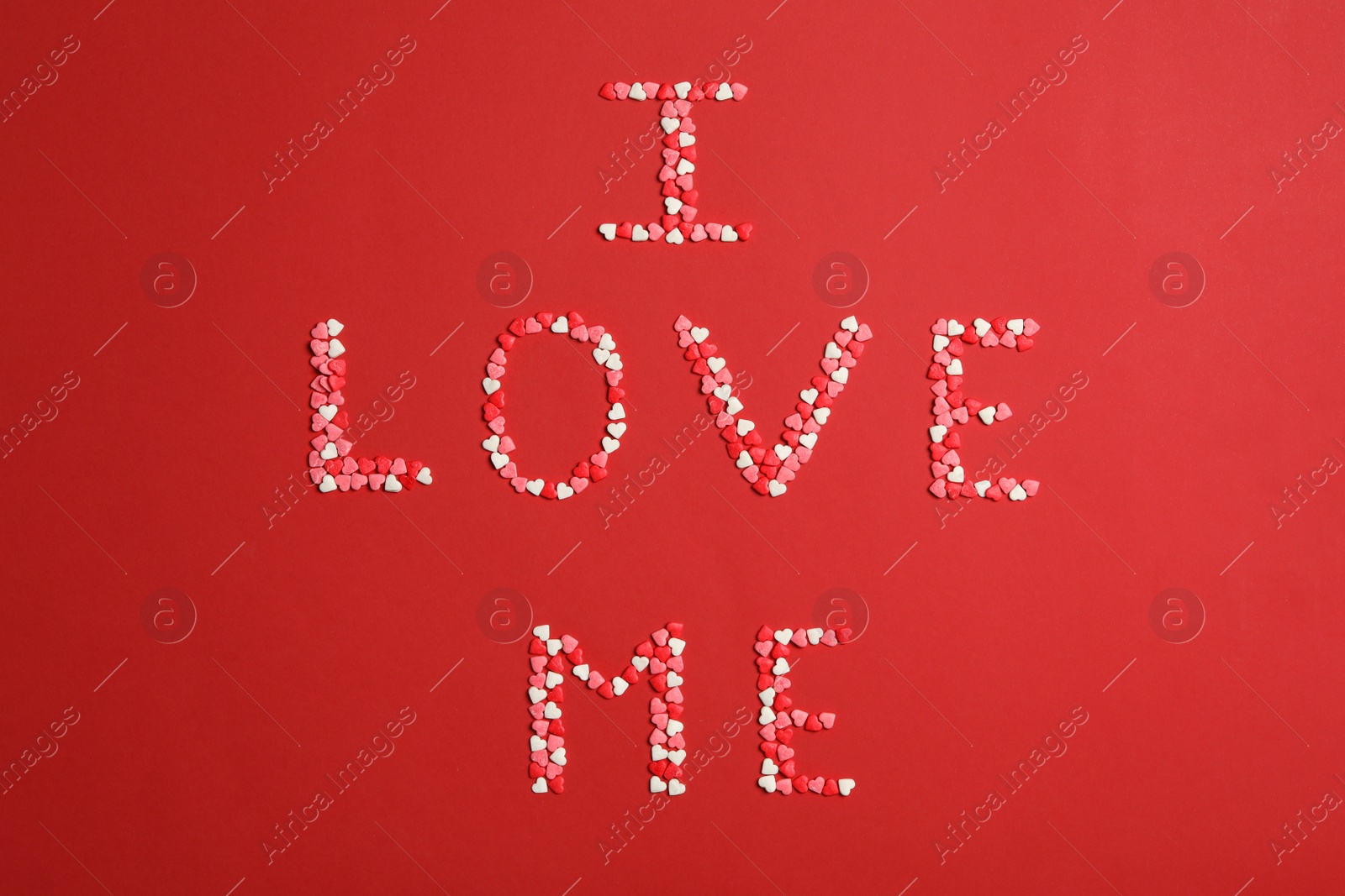 Photo of Phrase I Love Me made of heart shaped sprinkles on red background, flat lay