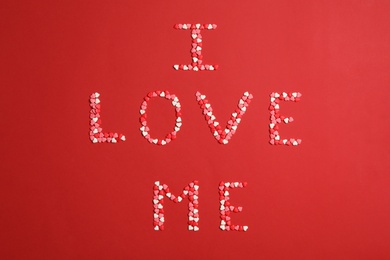 Phrase I Love Me made of heart shaped sprinkles on red background, flat lay