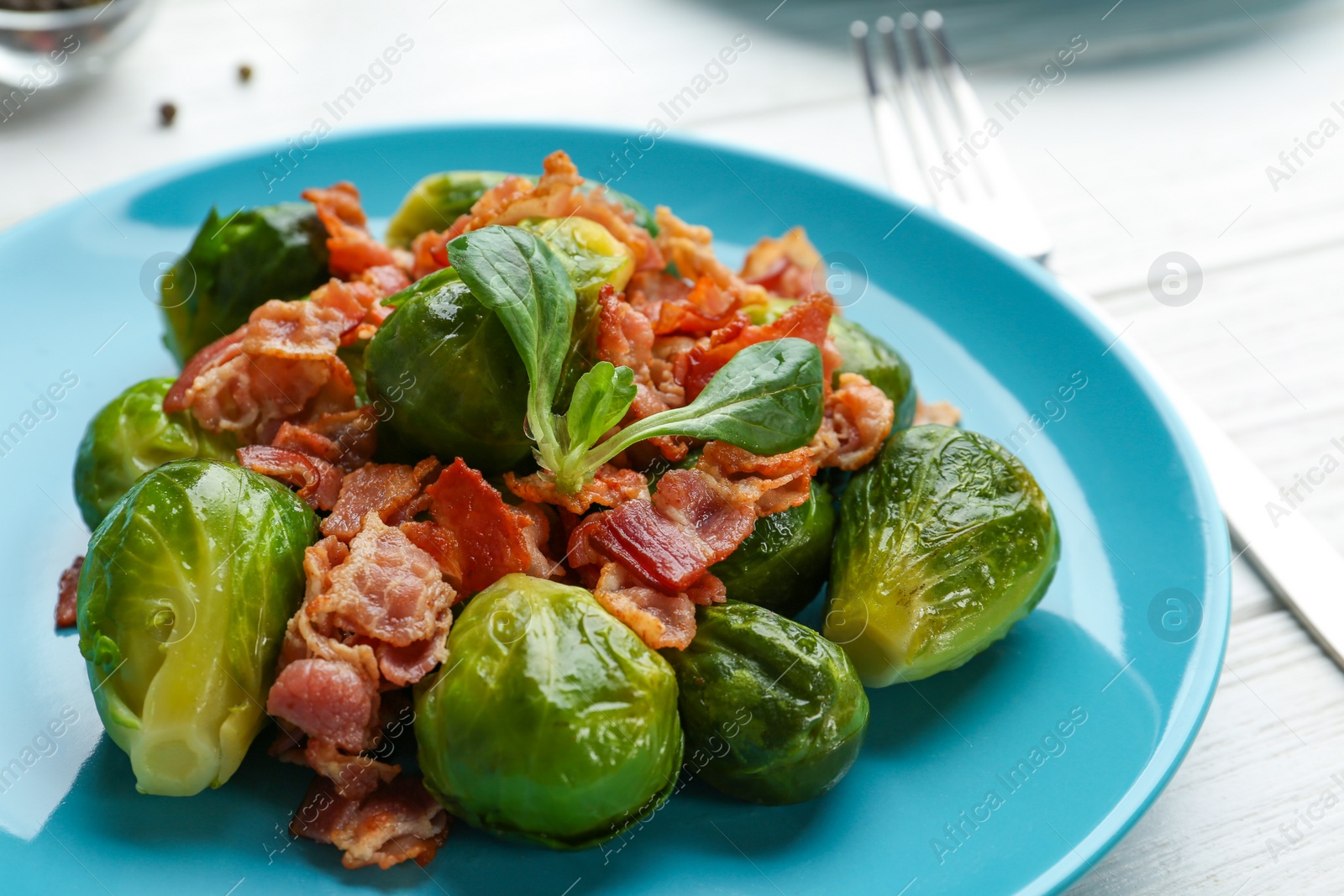 Photo of Tasty roasted Brussels sprouts with bacon on white wooden table, closeup