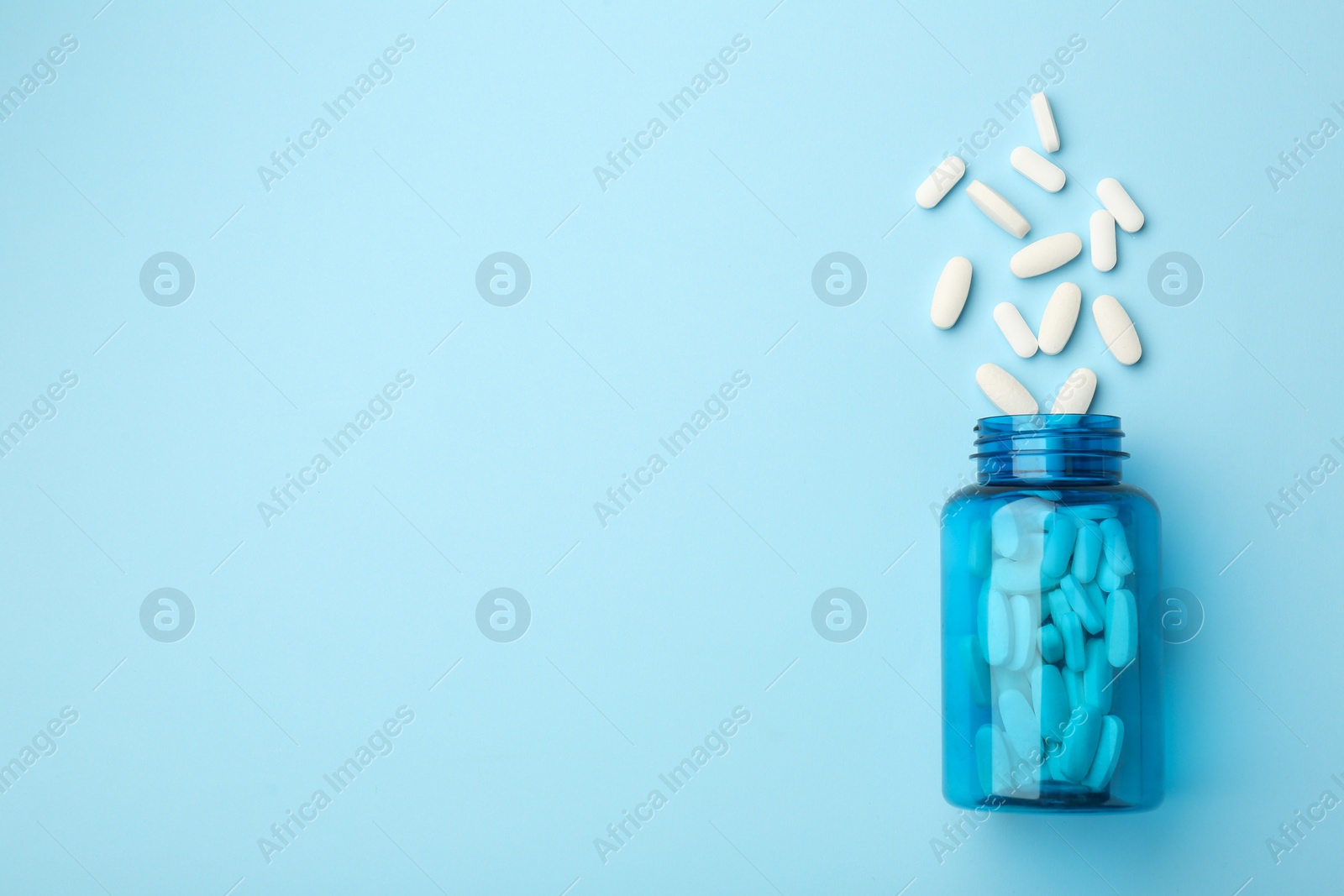 Photo of Vitamin pills and bottle on light blue background, top view. Space for text