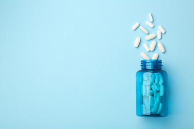 Photo of Vitamin pills and bottle on light blue background, top view. Space for text