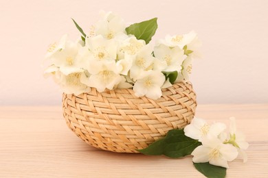 Photo of Beautiful jasmine flowers in wicker basket on wooden table