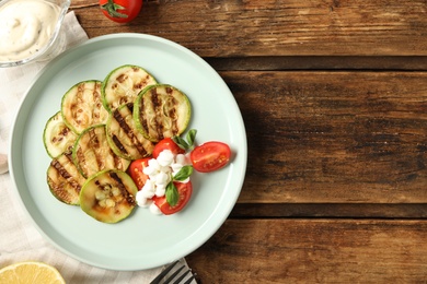 Photo of Delicious grilled zucchini slices served with cottage cheese and tomatoes on wooden table, flat lay. Space for text