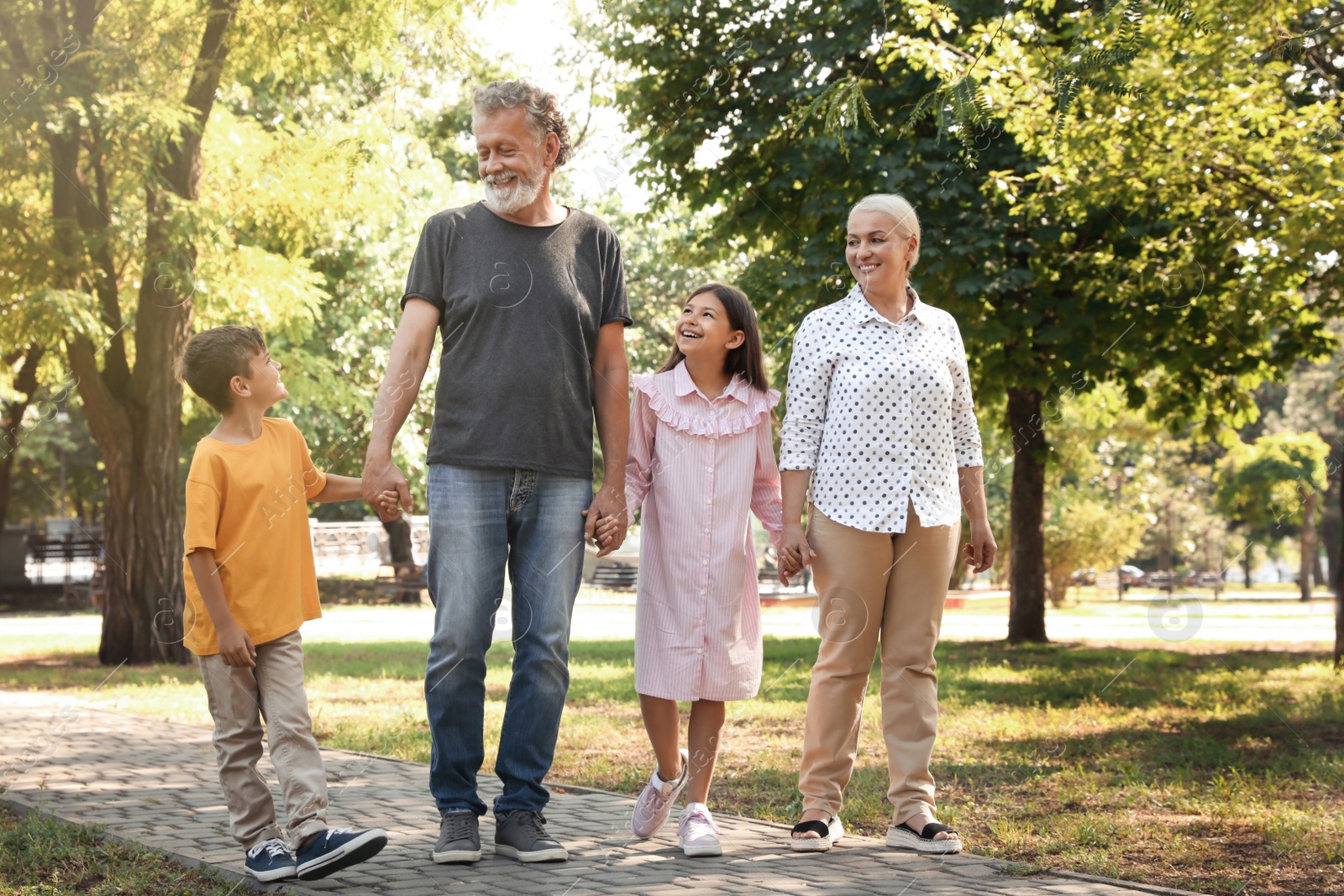 Photo of Happy grandparents with little children walking together in park