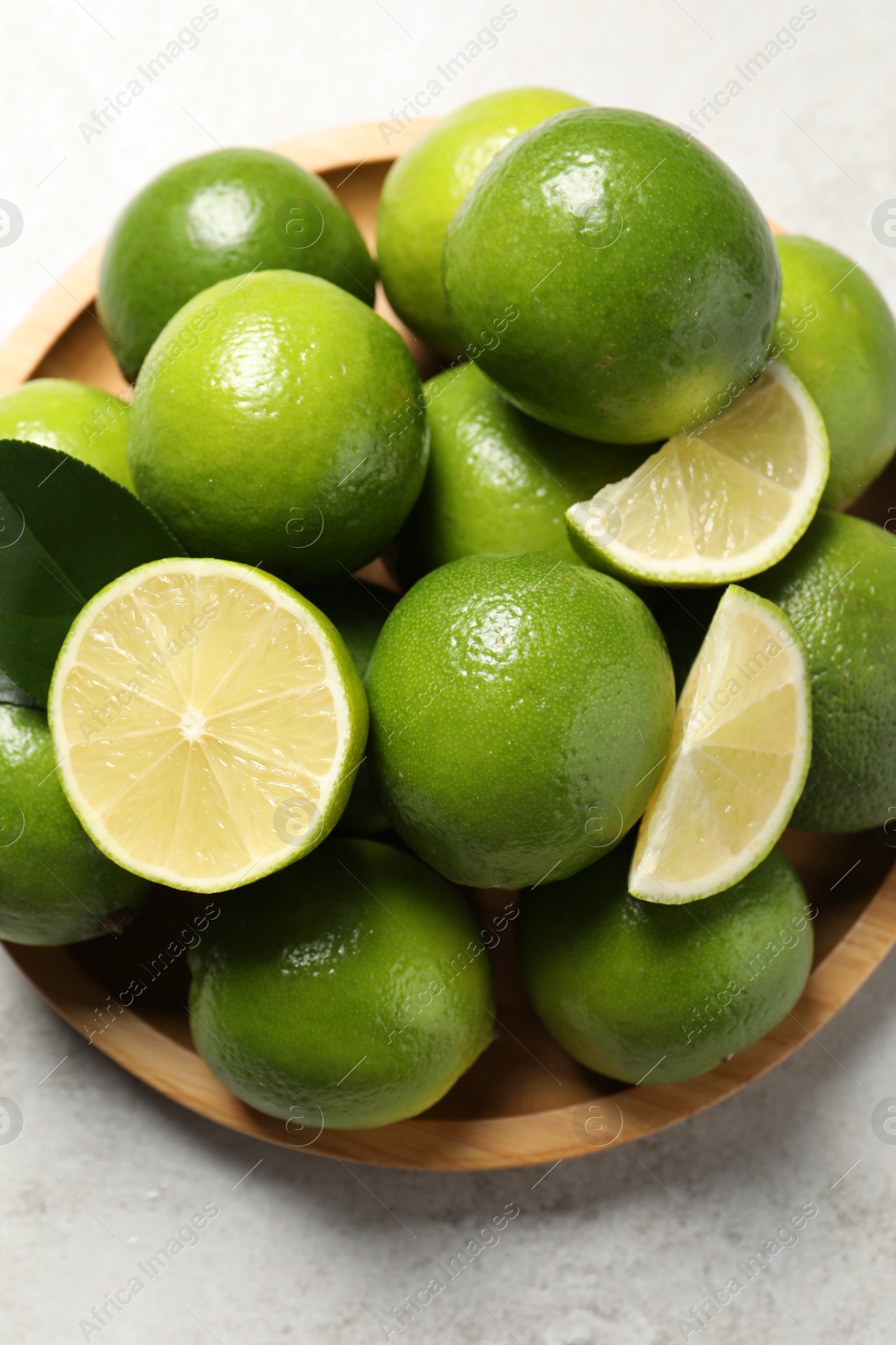 Photo of Fresh ripe limes and green leaves on light table, top view