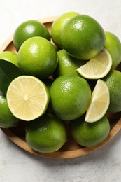 Fresh ripe limes and green leaves on light table, top view