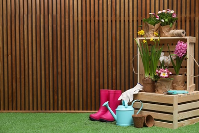 Composition with different gardening tools on artificial grass at wooden wall. Space for text