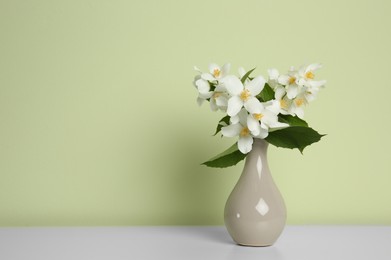 Bouquet of beautiful jasmine flowers in vase on table near light green wall, space for text