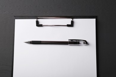 Photo of Clipboard with sheet of paper and pen on black wooden table, top view