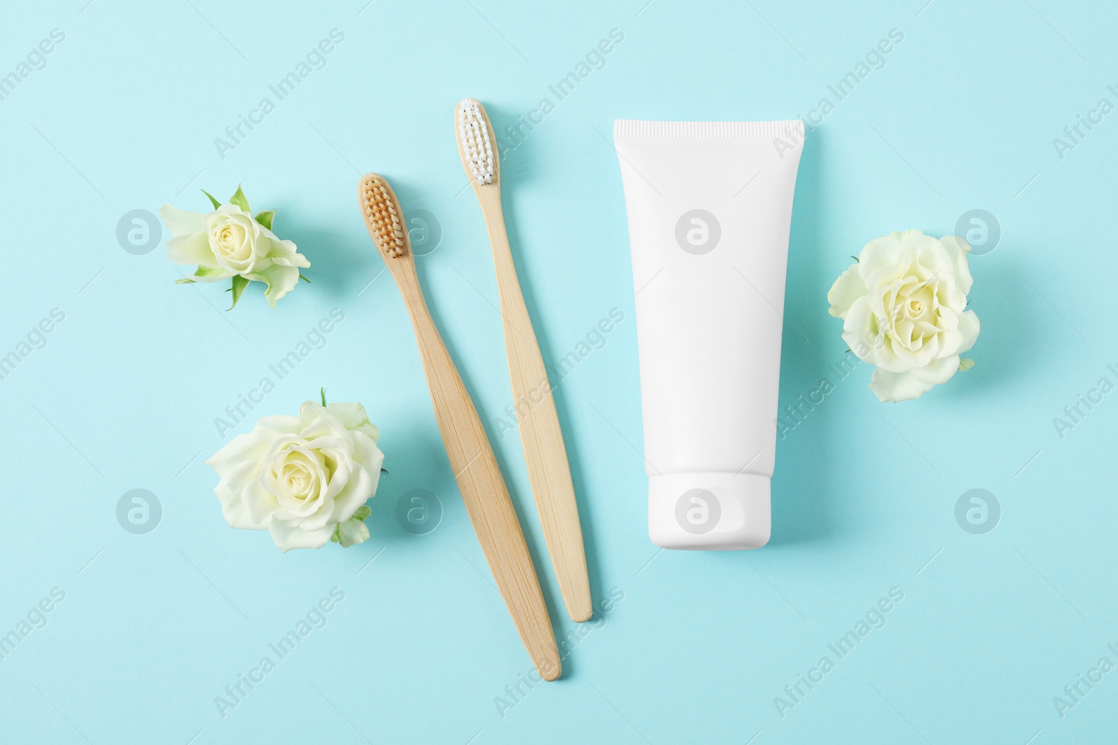 Photo of Flat lay composition with toothbrushes, toothpaste and flowers on turquoise background