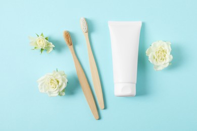 Photo of Flat lay composition with toothbrushes, toothpaste and flowers on turquoise background