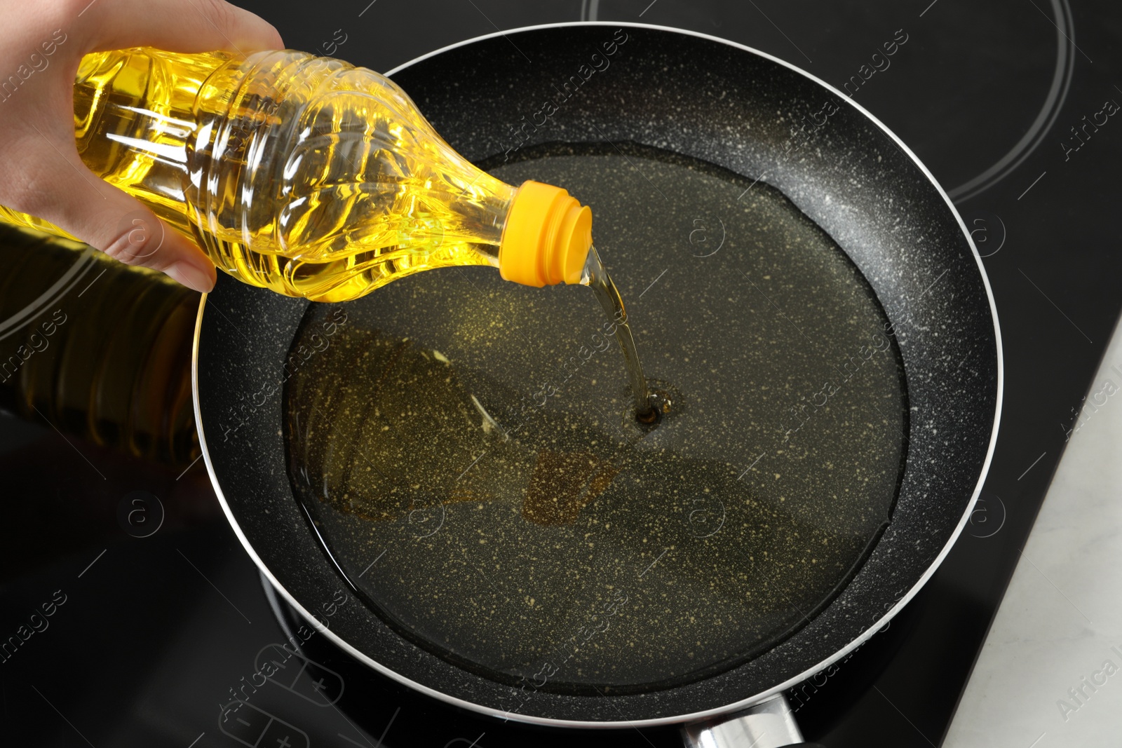 Photo of Woman pouring cooking oil from bottle into frying pan on stove, closeup