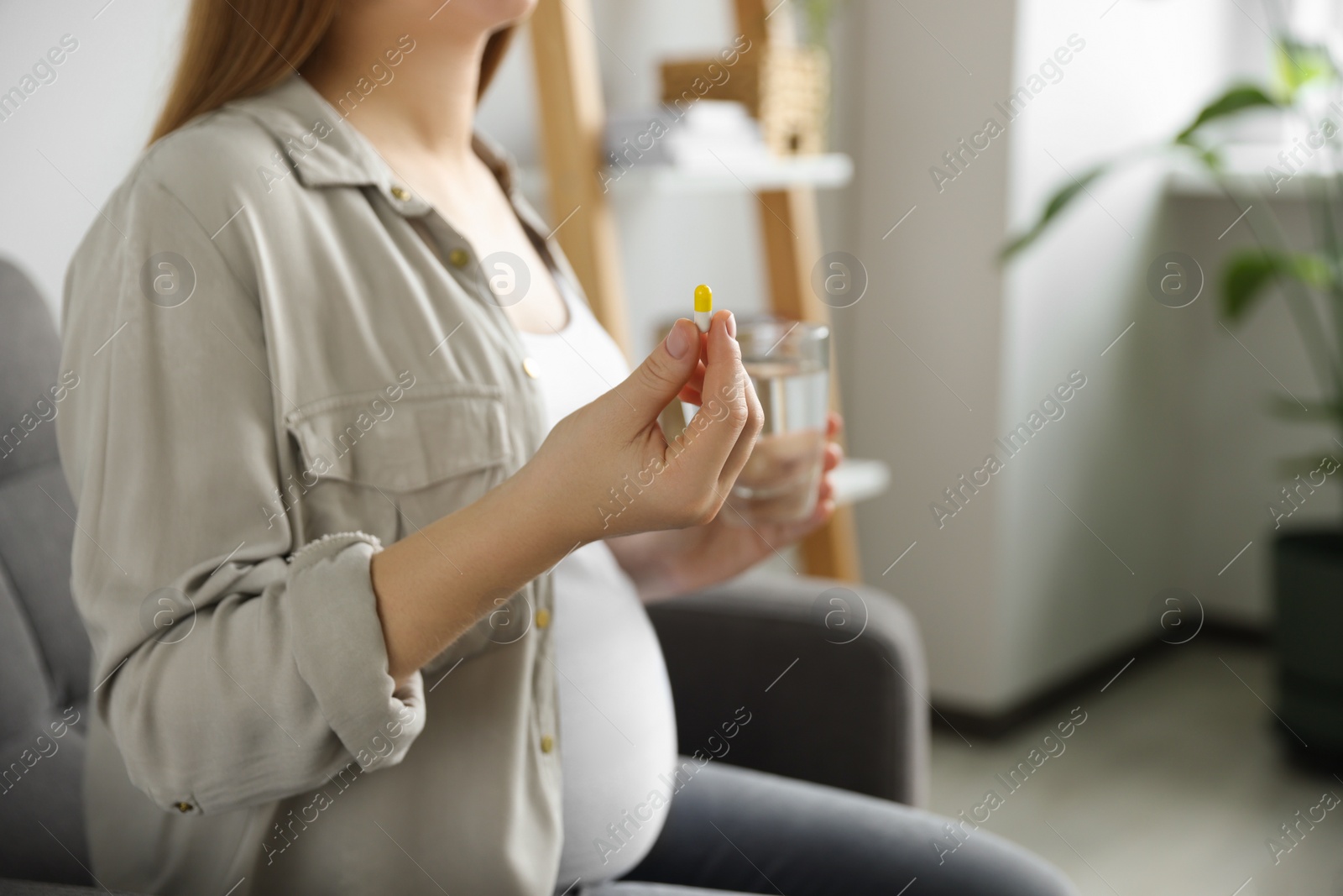 Photo of Pregnant woman holding pill and glass with water at home, closeup