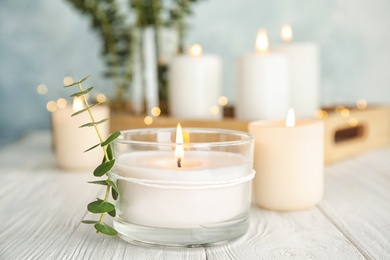 Photo of Burning aromatic candle and eucalyptus branch on table