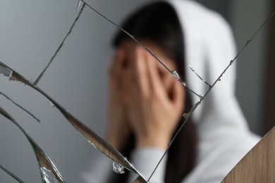 Photo of Woman covering face with hands near broken mirror. Mental problems