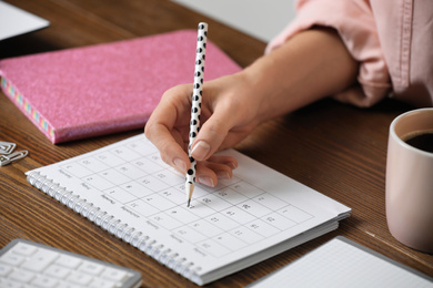 Photo of Woman marking date in calendar at wooden table, closeup