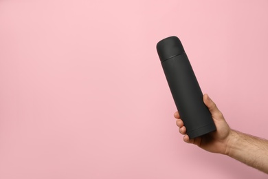 Photo of Man holding black thermos on pink background, closeup. Space for text