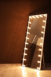 Stylish mirror with light bulbs near brown wall indoors. Interior element