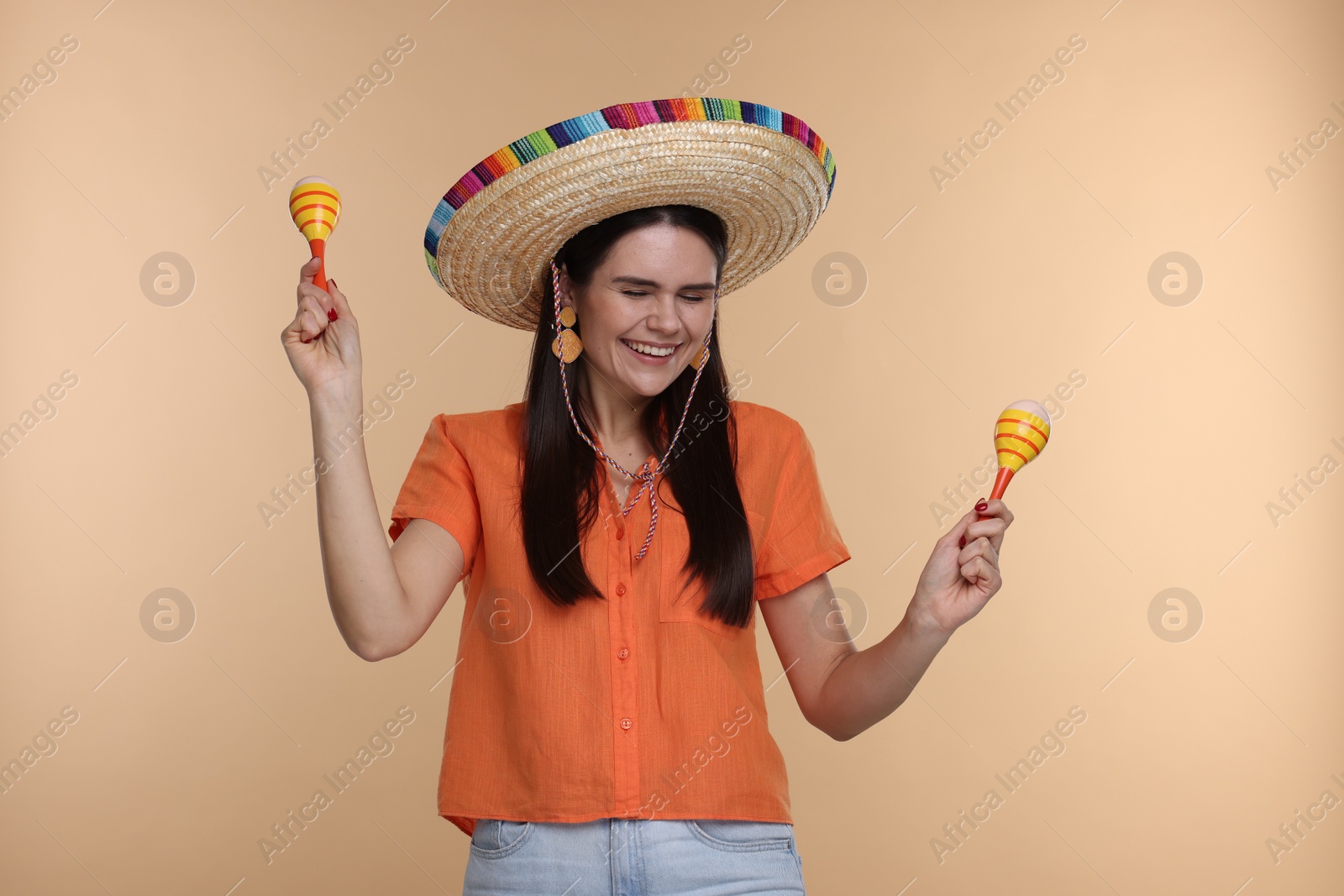 Photo of Young woman in Mexican sombrero hat with maracas on beige background