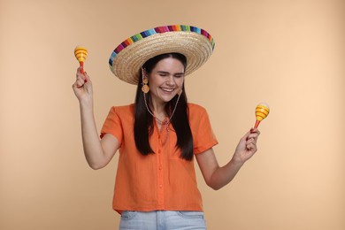 Young woman in Mexican sombrero hat with maracas on beige background