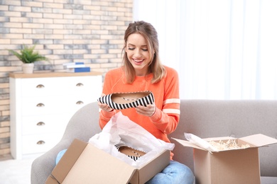 Photo of Young woman opening parcel on sofa in living room
