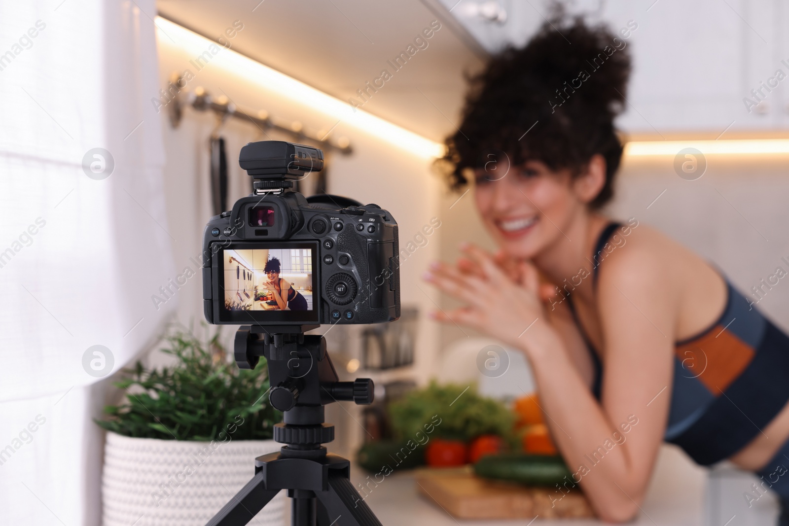 Photo of Food blogger explaining something while recording video in kitchen, focus on camera