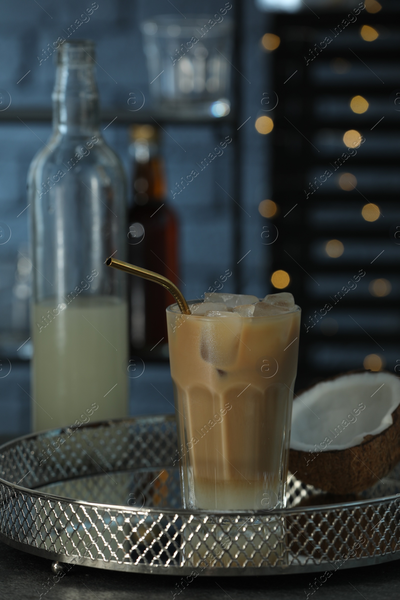 Photo of Delicious syrup, glass of iced coffee and coconut on grey table against blurred lights