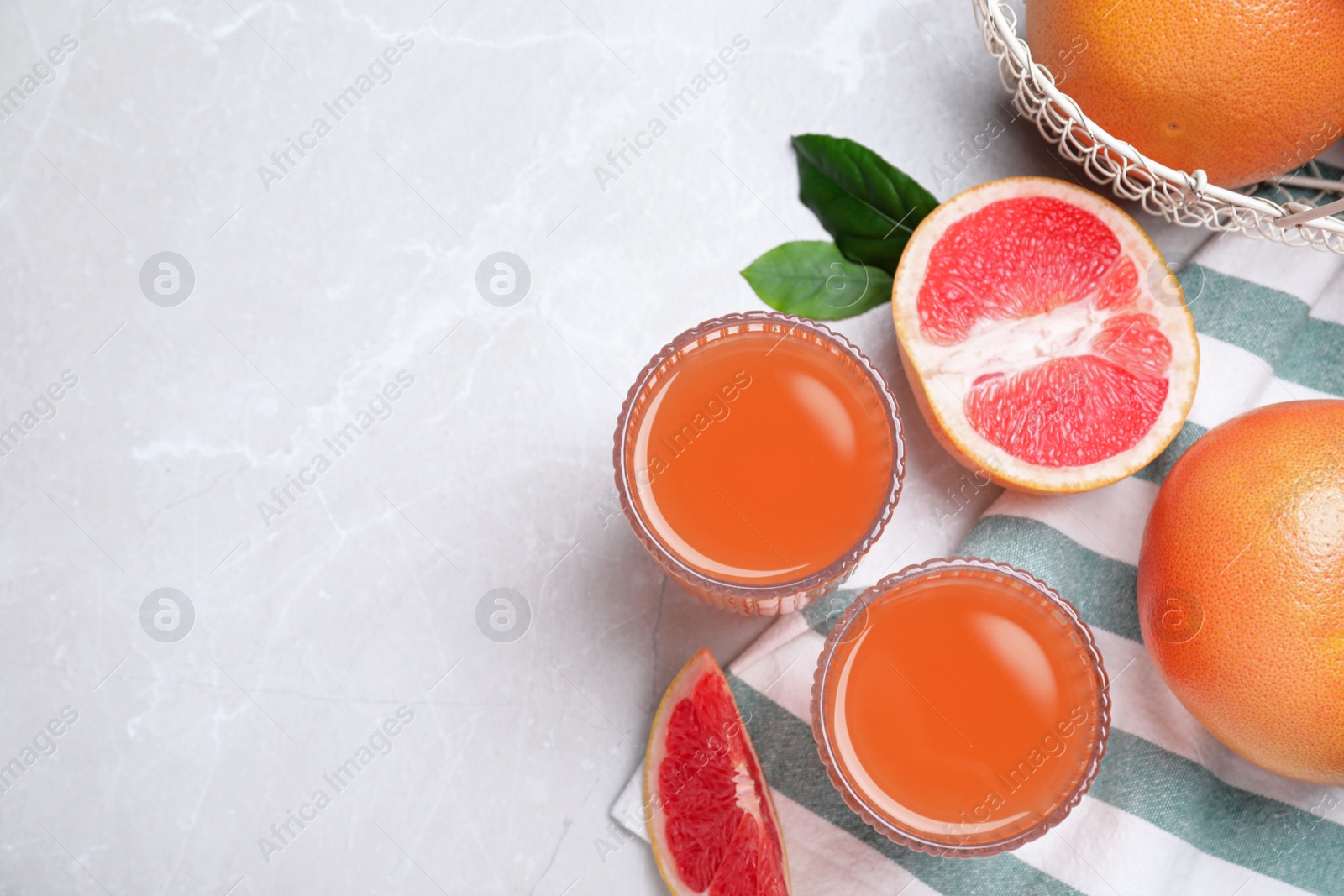 Photo of Tasty freshly made grapefruit juice and fruits on light grey marble table, flat lay. Space for text