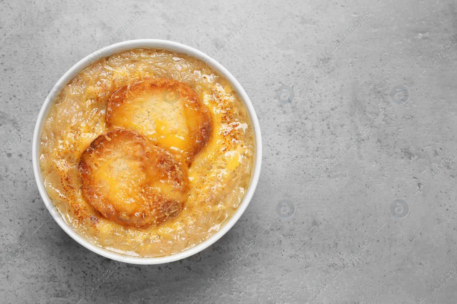 Photo of Tasty homemade french onion soup on grey table, top view. Space for text