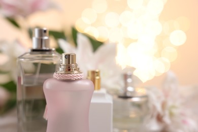 Photo of Bottlesperfume against beautiful lily flowers and blurred lights, closeup. Space for text