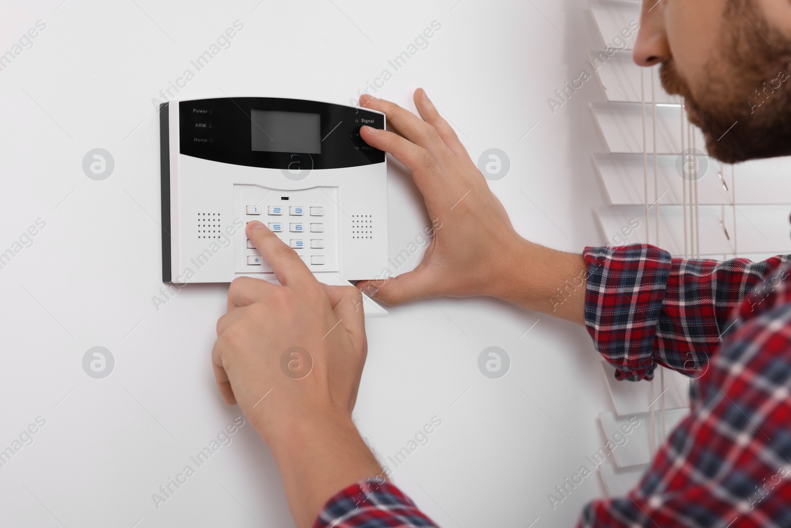 Photo of Man entering code on security alarm system at home, closeup