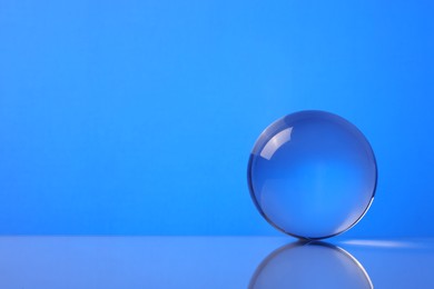 Photo of Transparent glass ball on mirror surface against blue background. Space for text