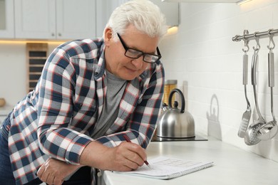 Senior man solving sudoku puzzle at kitchen counter