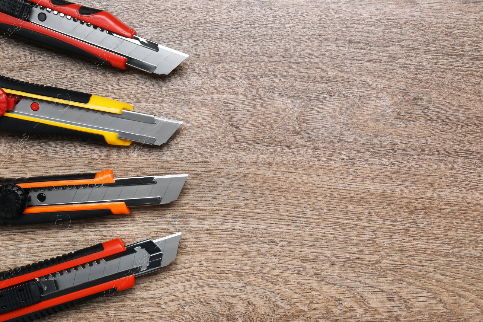 Photo of Many different utility knives on wooden table, flat lay. Space for text