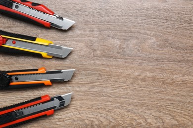 Photo of Many different utility knives on wooden table, flat lay. Space for text